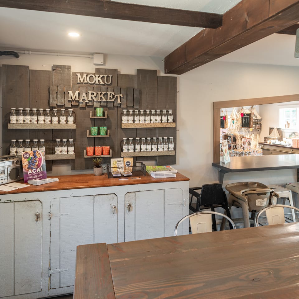 Rustic Moku Market café interior with shelves of bottled products, wooden counters, exposed beams, and communal dining tables.