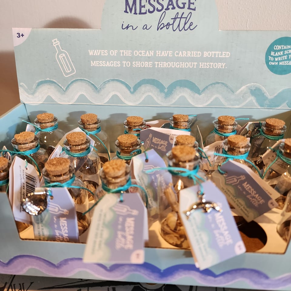 Display of corked glass message bottles with turquoise ribbons beneath a sign reading “Message in a Bottle.”