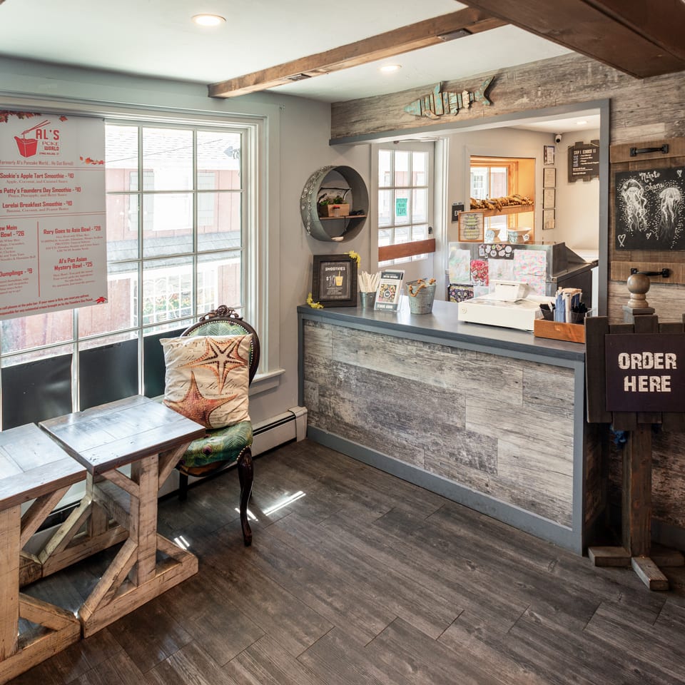 Rustic Al’s Poke World restaurant interior with wooden tables, ordering counter, menu board, and coastal-themed decor.