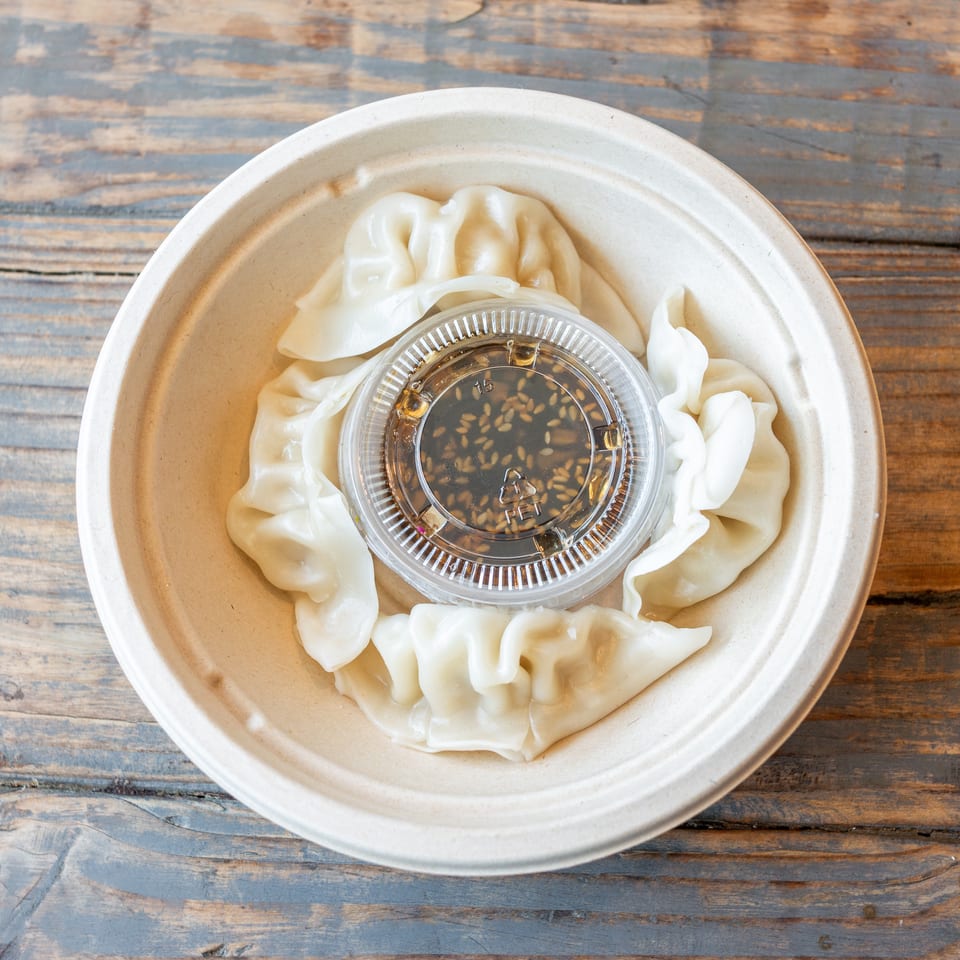 Steamed dumplings arranged around a clear cup of sesame dipping sauce on a rustic wooden table.