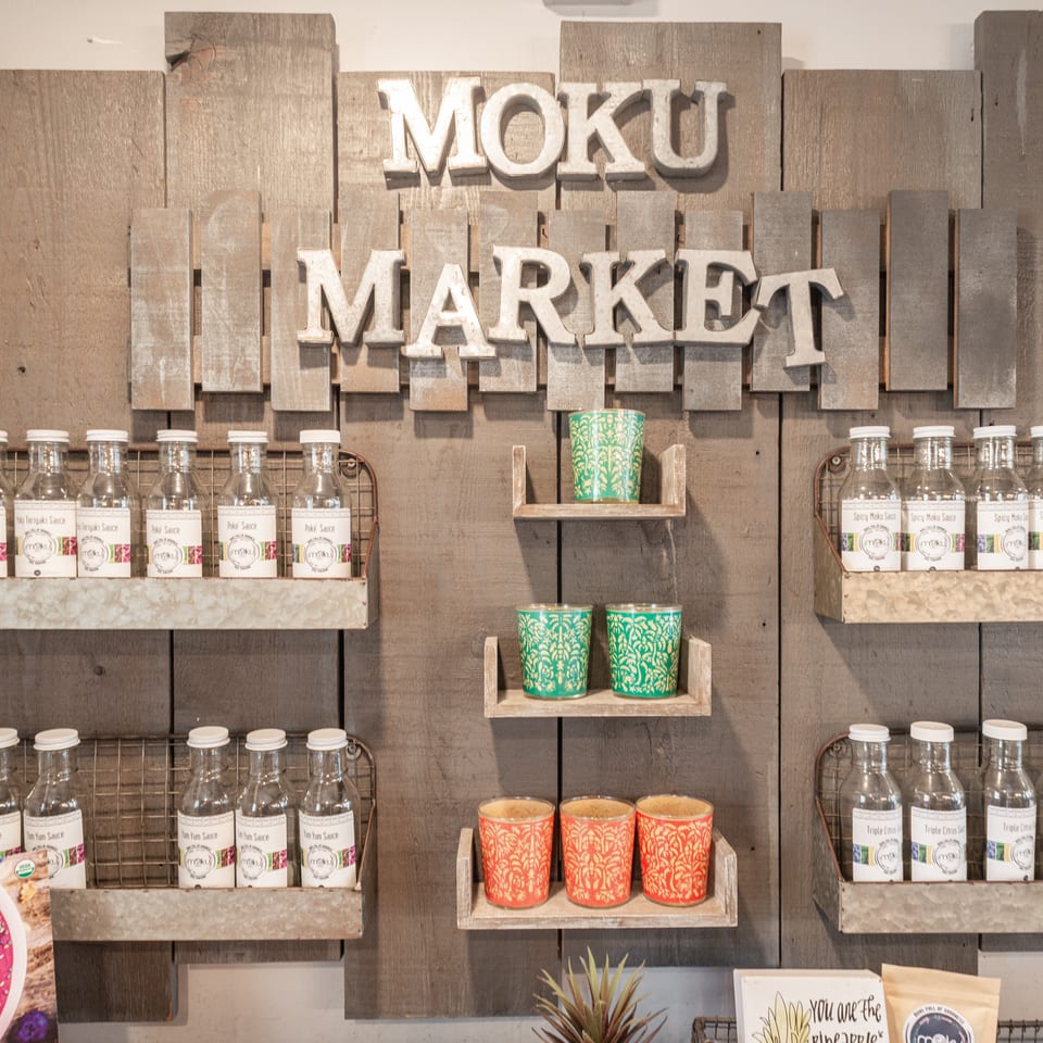 Rustic Moku Market display featuring sauce bottles, colorful patterned cups, and wooden wall signage.