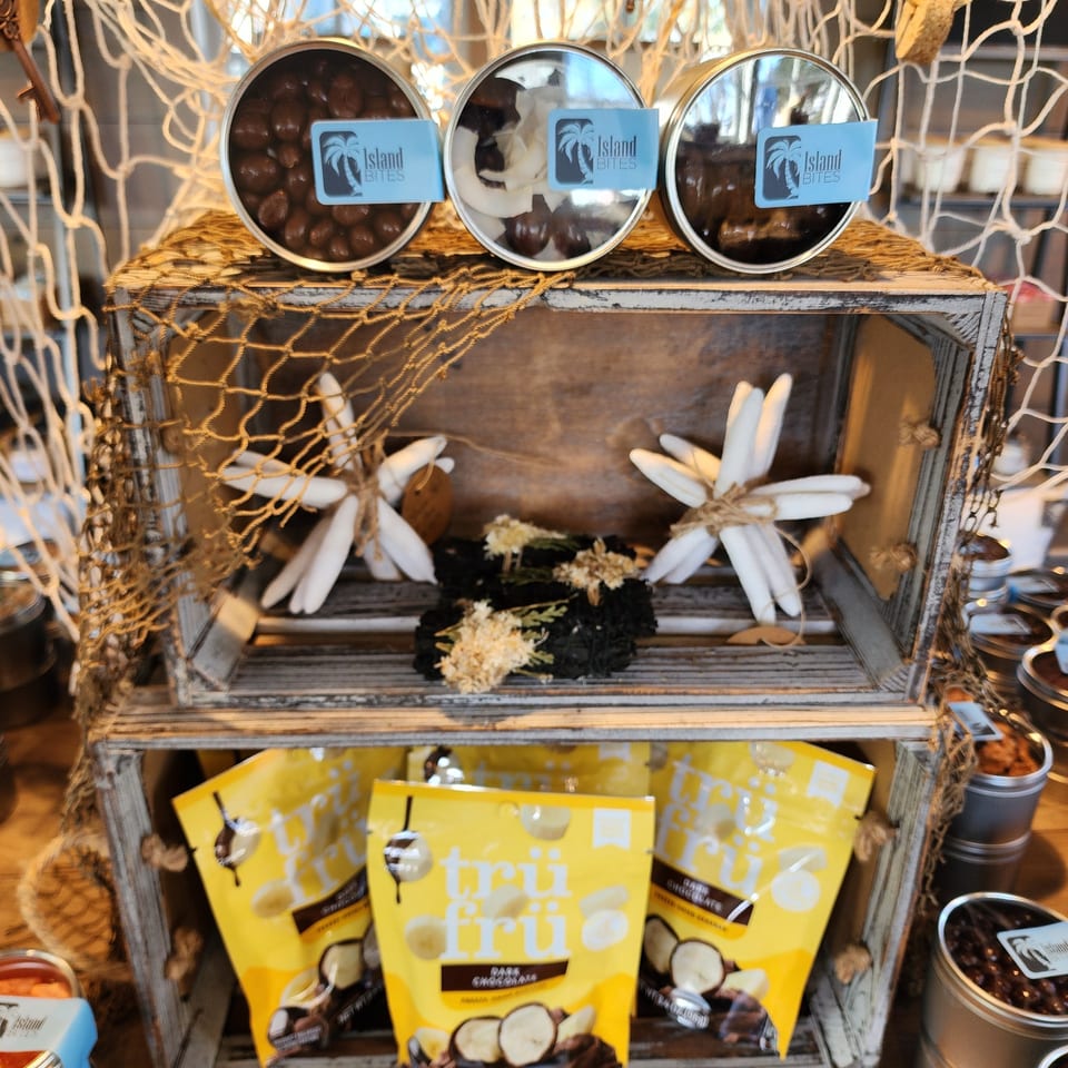 Island Bites display featuring jars of chocolate-covered snacks and yellow fruit treat packages on a rustic wooden shelf.