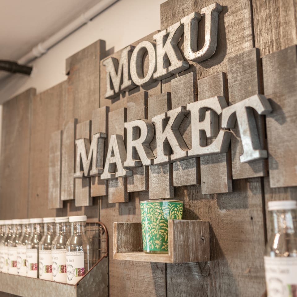 Rustic wooden wall displays a raised “MONKEY MARKET” sign above shelves of bottled products and a green patterned cup.