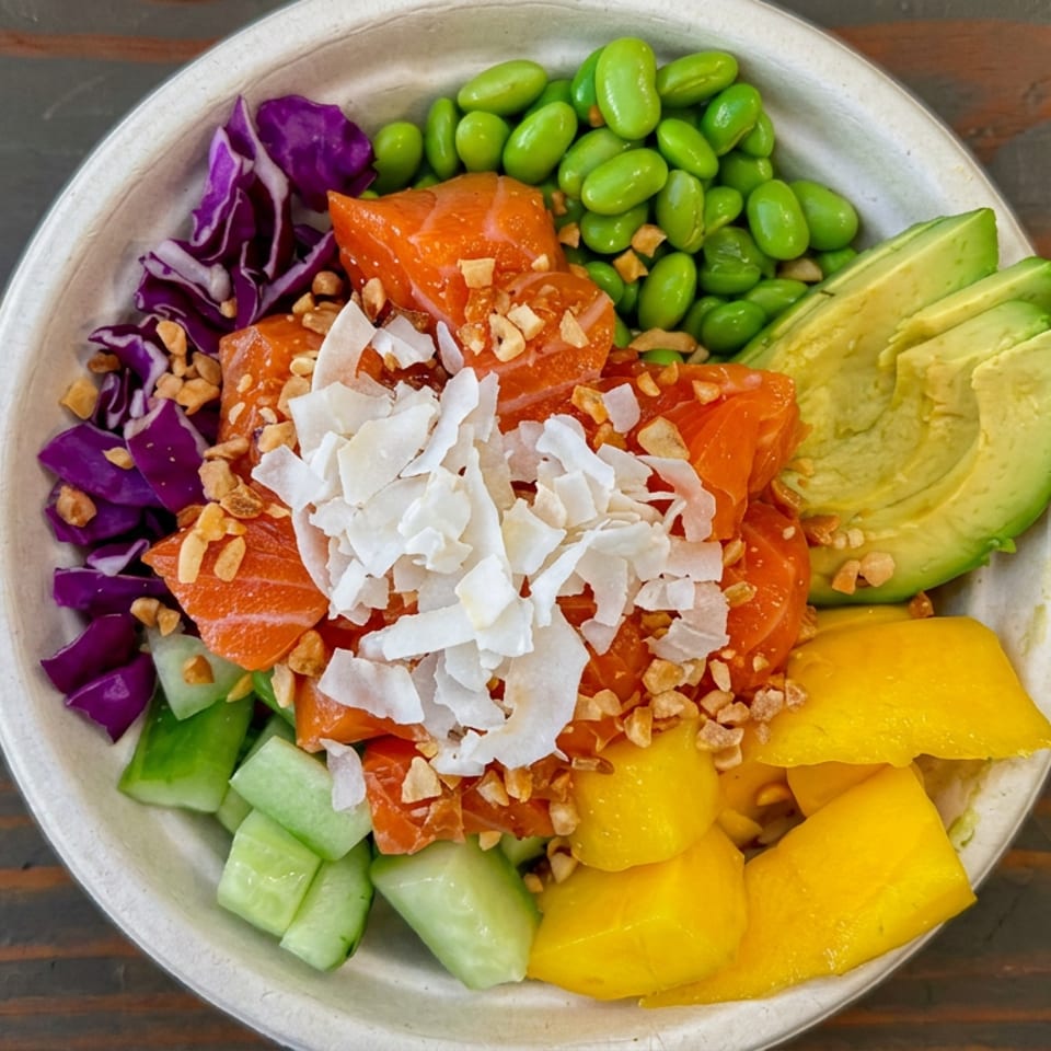 Colorful salmon poke bowl with edamame, avocado, mango, cucumber, purple cabbage, coconut flakes, and crunchy toppings.