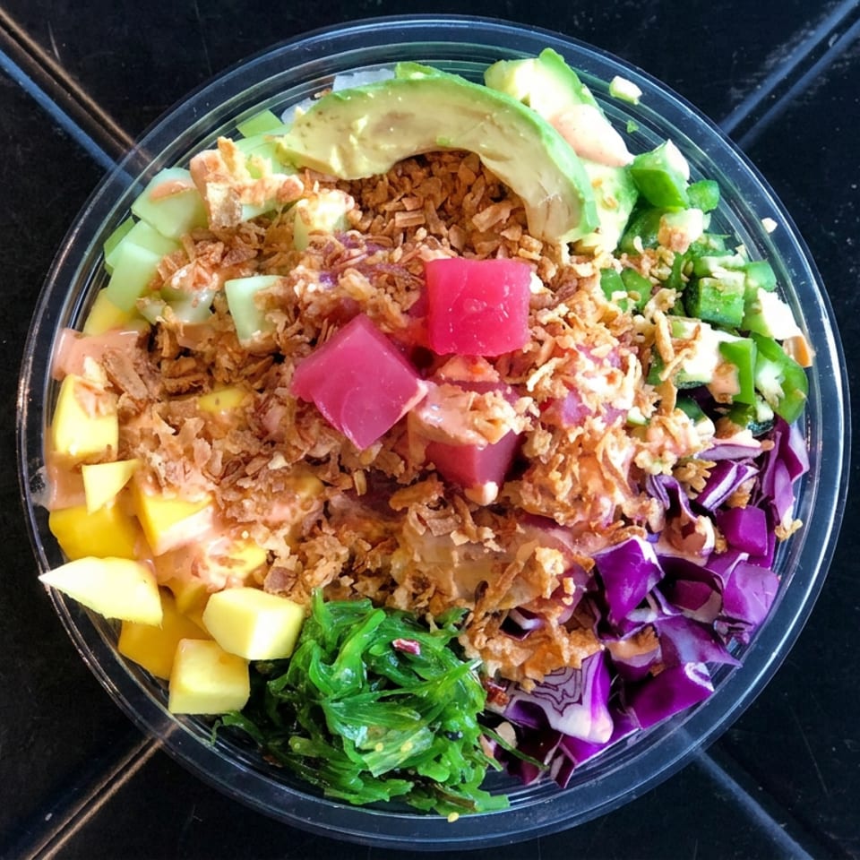 Colorful poke bowl topped with avocado, crispy onions, pickled radish, mango, cucumber, seaweed, and purple cabbage.
