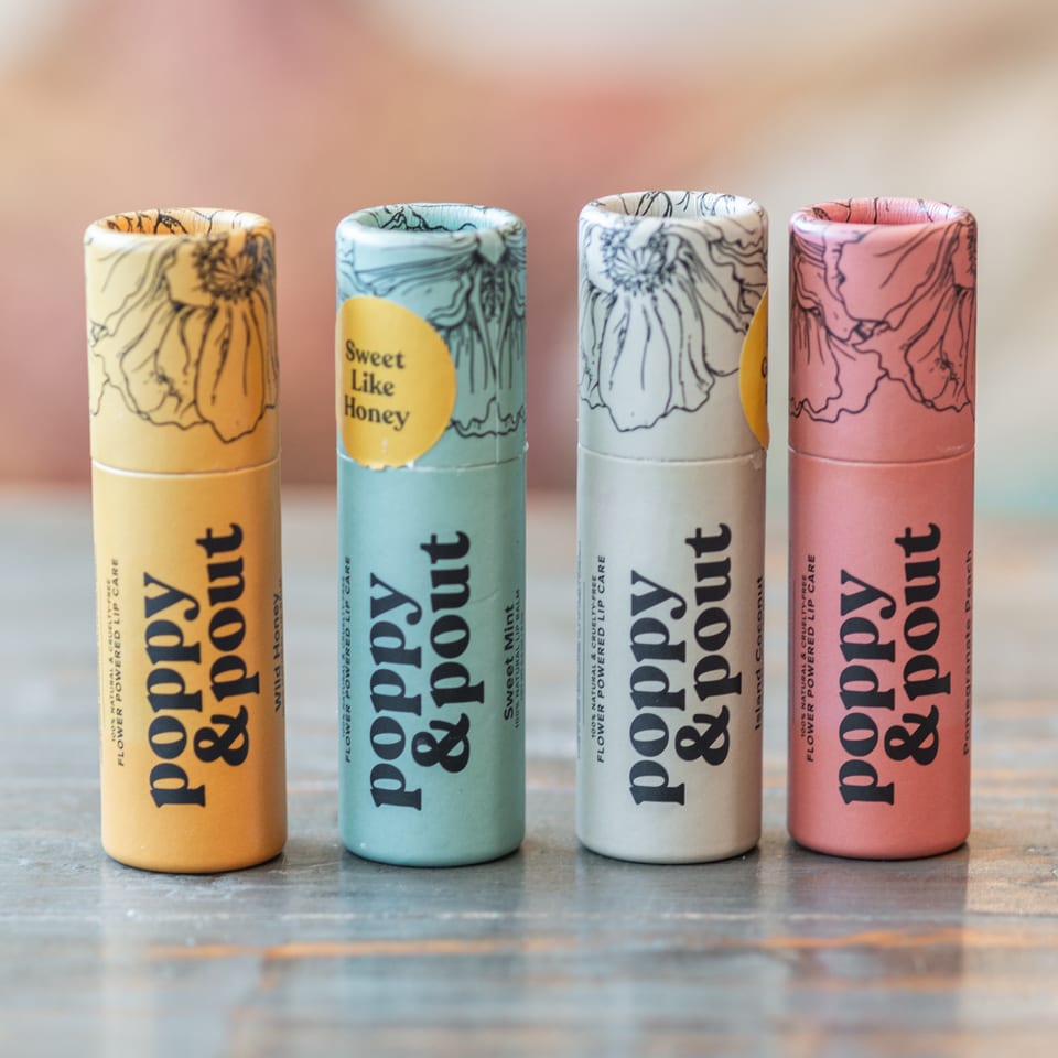 Four colorful PopSockets lip care tubes with floral designs arranged on a reflective tabletop.